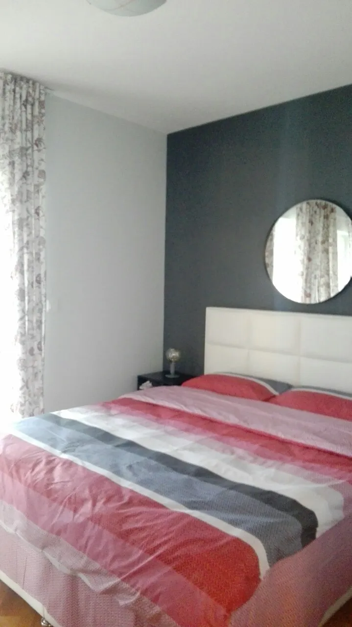 Schlafzimmer mit Bett, Kopfteil und Spiegel an der dunklen Wand.