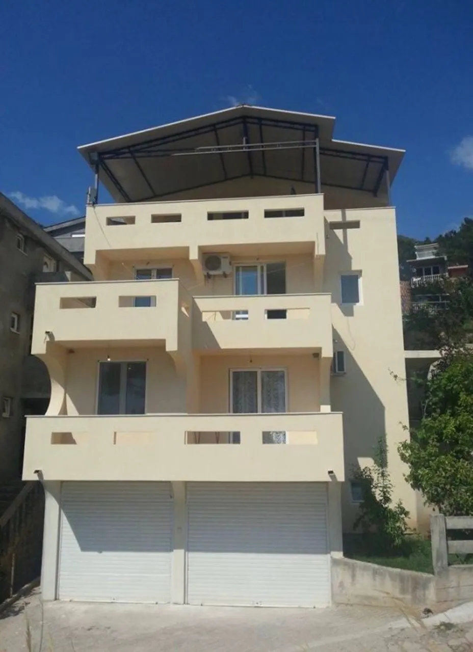 Vue extérieure d'un immeuble résidentiel à plusieurs étages avec balcons, portes de garage blanches et toiture.