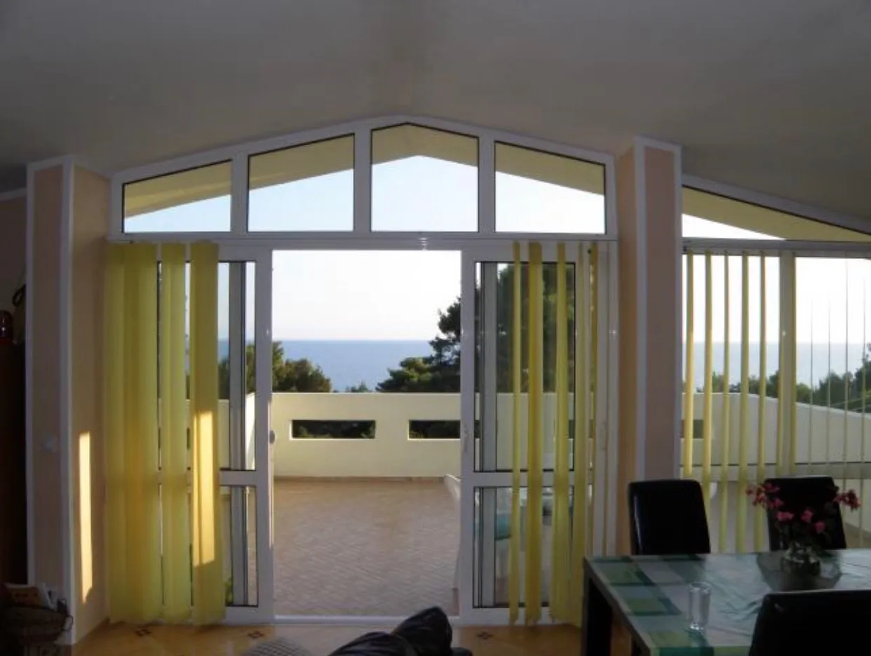 Salon avec grandes fenêtres en arc de cercle donnant sur une terrasse avec vue sur la mer. Table à manger visible.