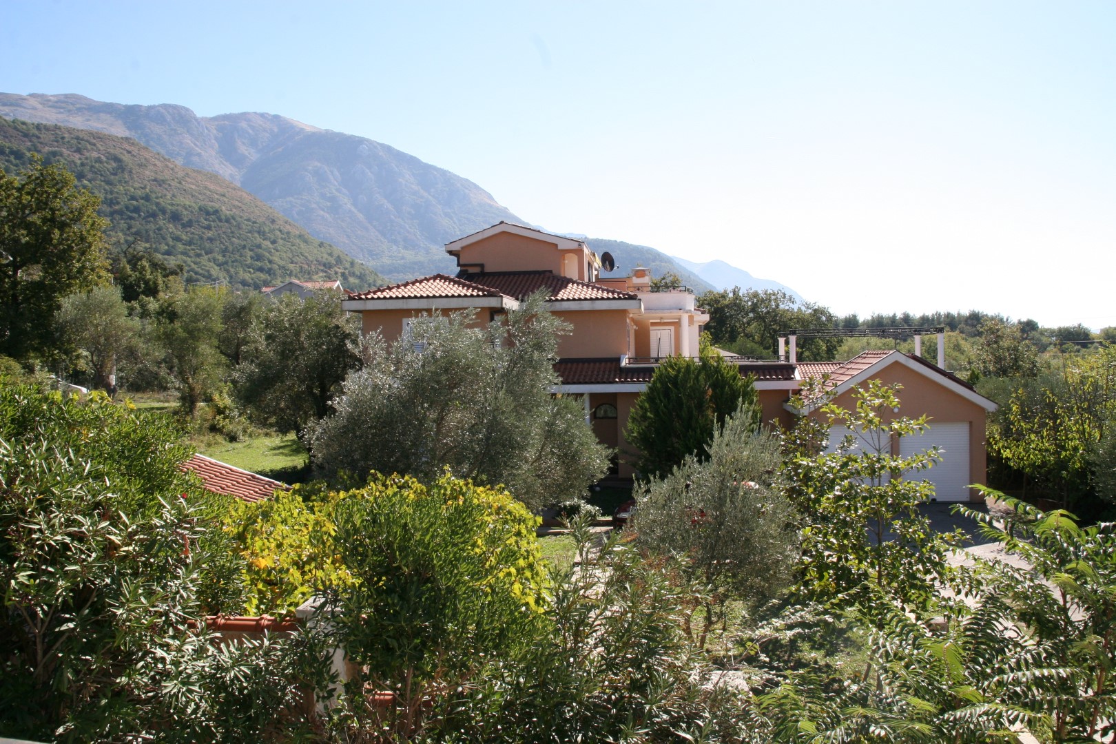 Dvospratna vila sa garažom u Kavaču, Crna Gora, sa planinama u pozadini u Bokokotorskom zalivu, okružena zelenilom i maslinama.
