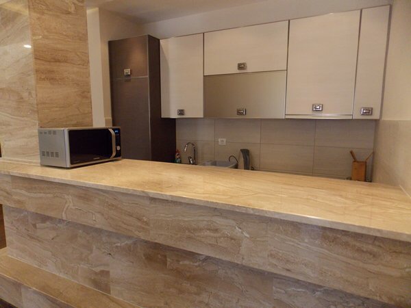 Moderne Küche mit Marmor-Bar in einer Wohnung in Budva, Montenegro: weiße Fronten und Einbaugeräte.