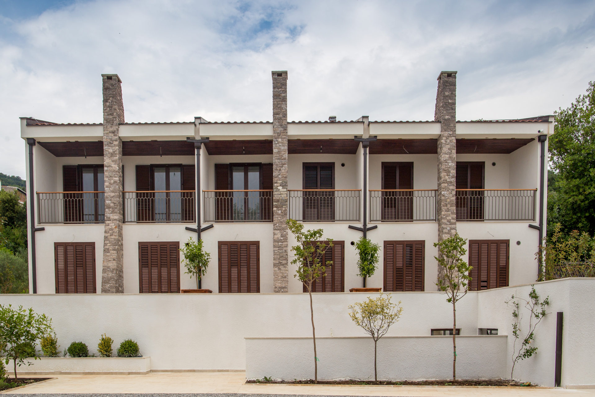 Fassade eines modernen Wohnkomplexes in Tivat, Montenegro: weiße Wände, Steinsäulen und Holzläden an den Fenstern.