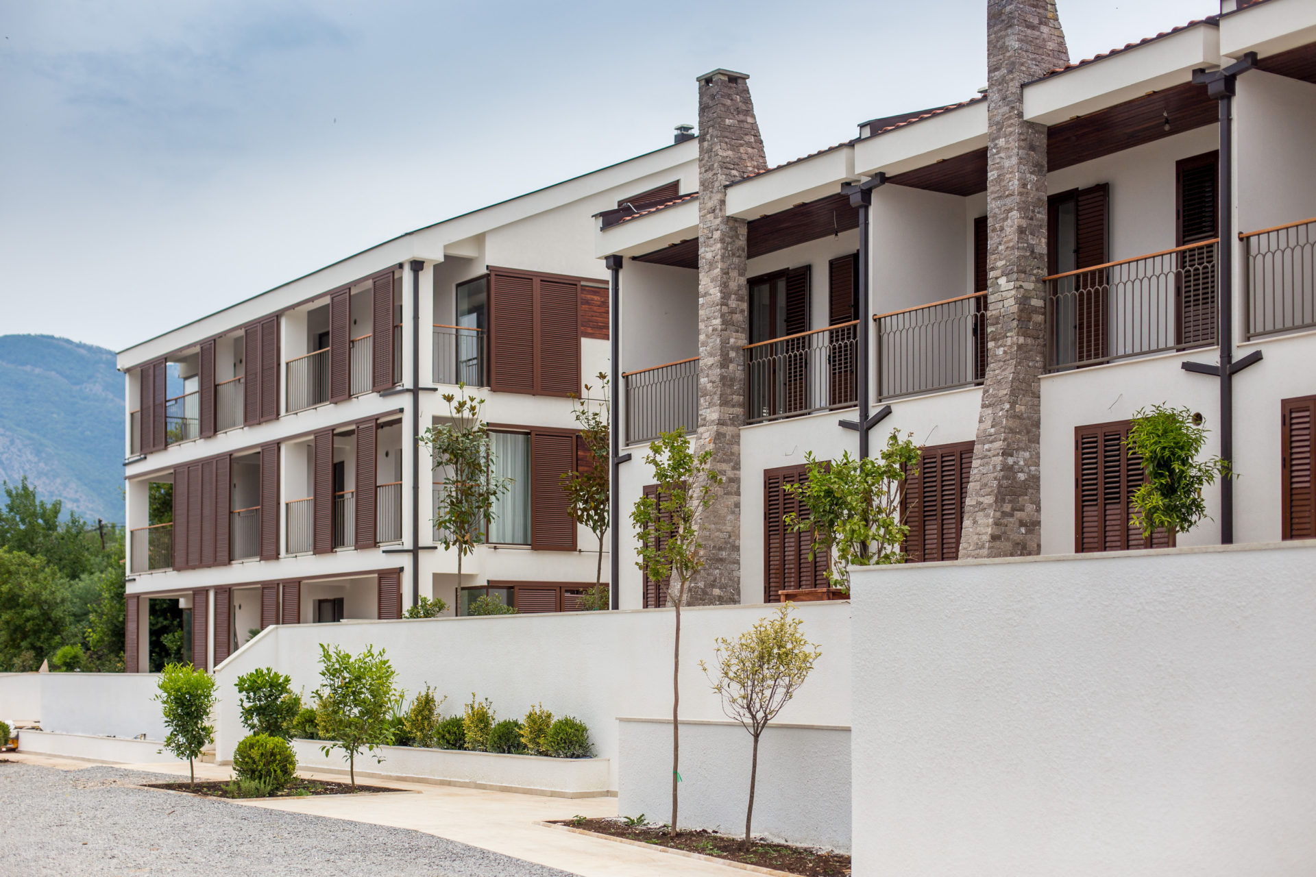 Moderner Wohnkomplex in Tivat, Montenegro: weiße Fassaden, Balkone mit Steinverkleidung und grüne Landschaftsgestaltung.