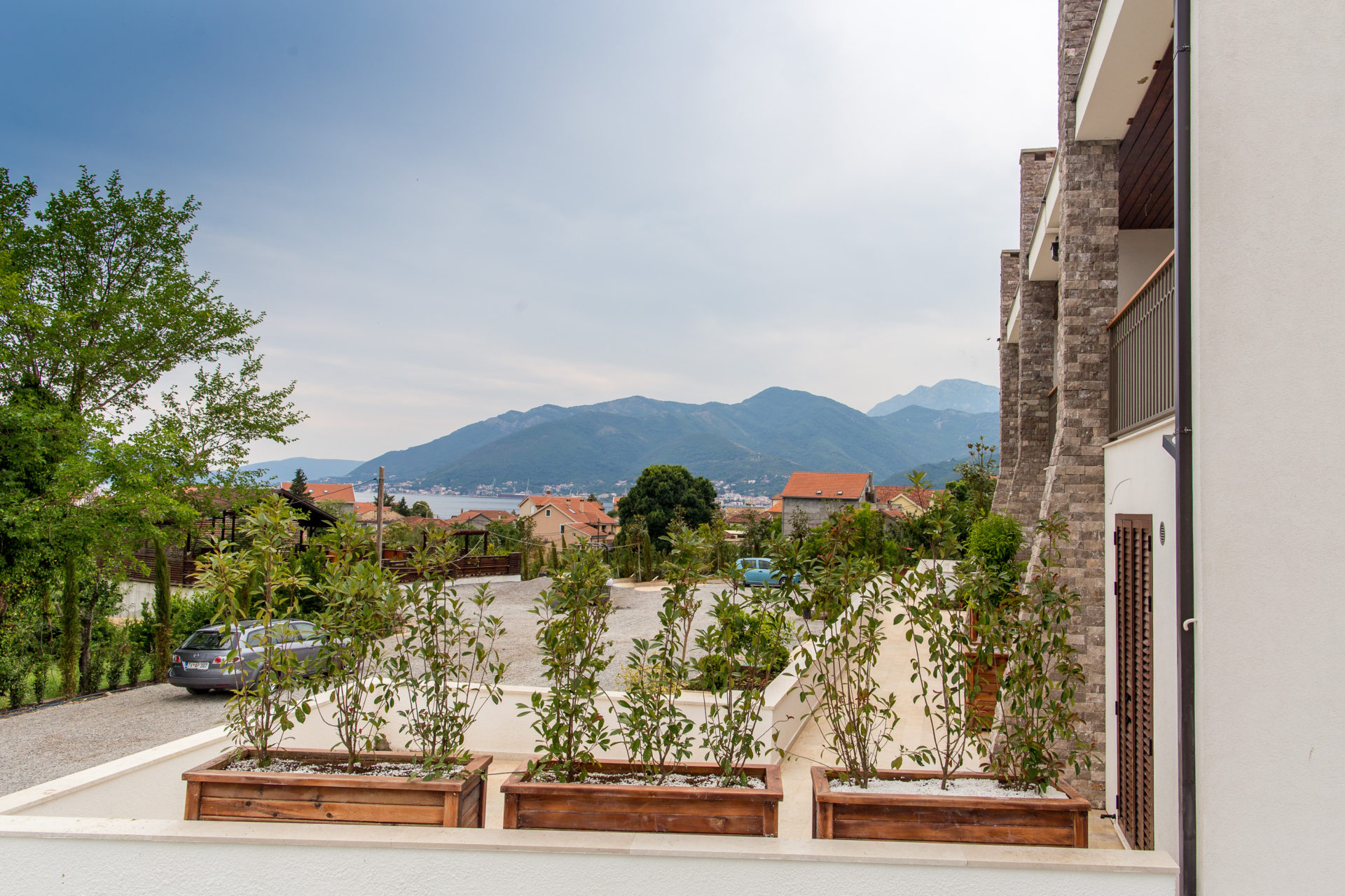 Blick vom Balkon einer modernen Wohnung in Tivat, Montenegro: Steinfassade, Grünanlagen und Berge.