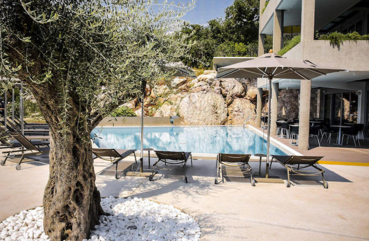 Pool an einer modernen Villa in Kamenovo, Montenegro: Sonnenliegen, Sonnenschirme und ein Olivenbaum auf der Terrasse am Felsen.