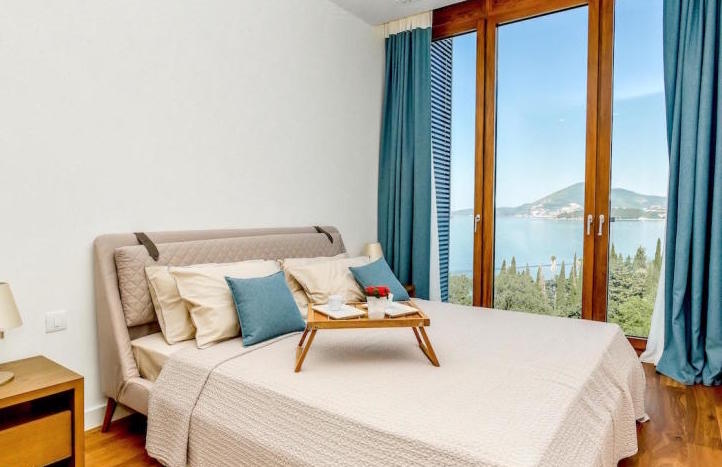 Schlafzimmer in einer Wohnung in Kamenovo, Montenegro: Doppelbett, Panoramafenster mit Blick auf das Meer und die Berge.
