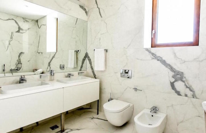 Modernes Badezimmer mit weißer Marmoroptik in einer Wohnung, Kamenovo, Montenegro: zwei Waschbecken und Sanitäranlagen.