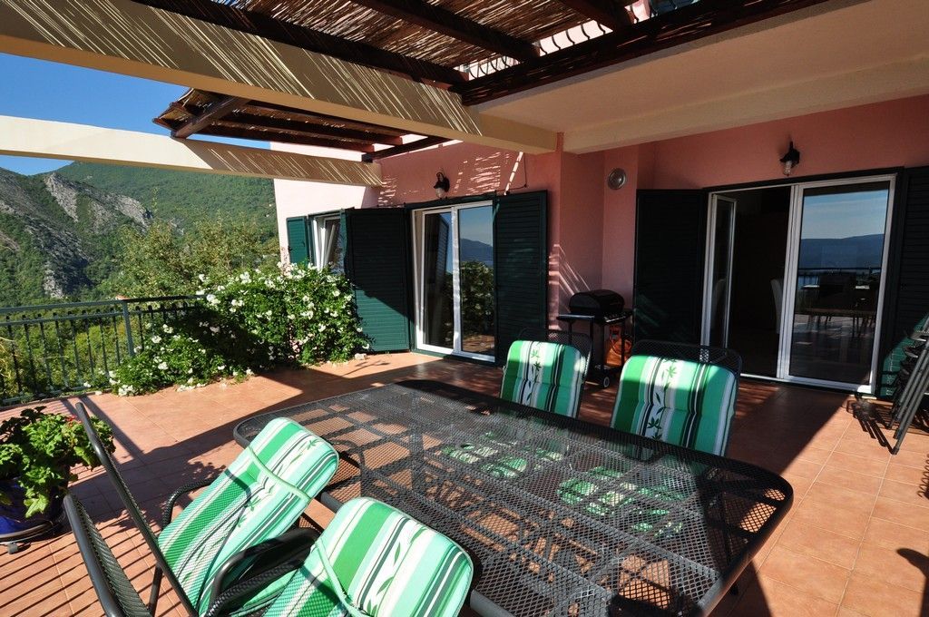 Terrasse der Villa in Tivat, Montenegro: Essbereich, Überdachung, Bergblick und Panoramatüren mit grünen Fensterläden.