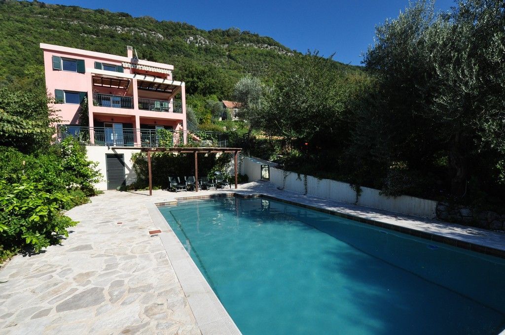 Rosa Villa mit Pool und Terrasse in Tivat, Montenegro: Blick auf das Haus, den Ruhebereich und die Berglandschaft.