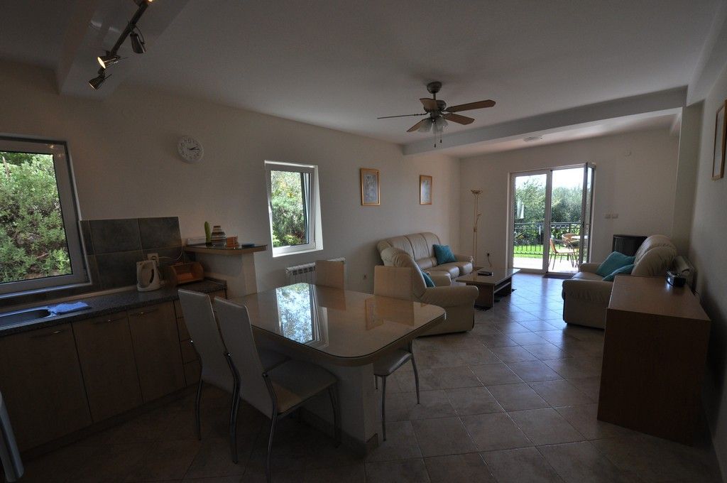Wohnzimmer mit Küche und Zugang zur Terrasse in einer Villa, Tivat, Montenegro: helle Möbel, Fliesenboden und Blick auf den Garten.
