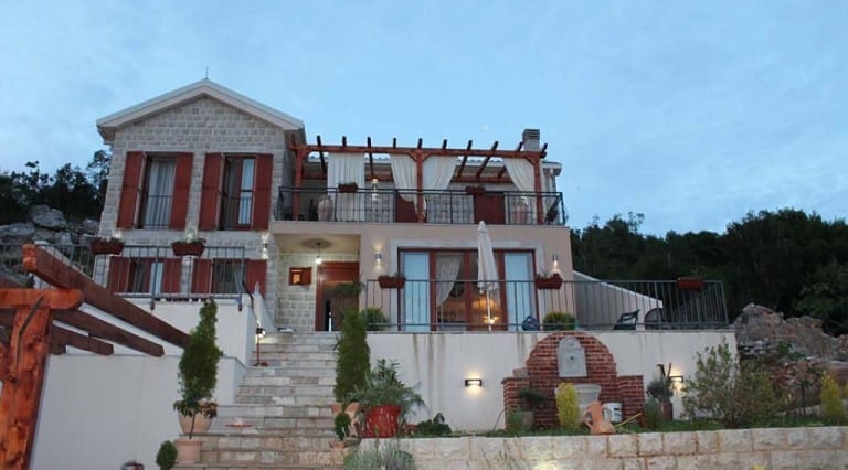 Krymovice, Karadağ’da teraslı ve pergolalı iki katlı taş villa: merdiven ve bahçeli cephe görünümü.