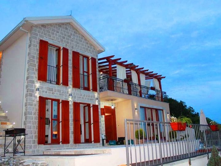 Karadağ, Krimovitsa’da iki katlı villa: taş cephe kaplaması, kırmızı panjurlar ve ahşap pergolalı teras.