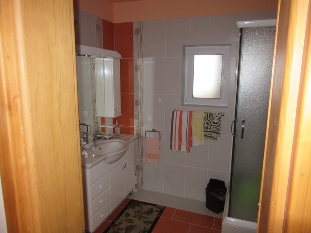 Salle de bains avec cabine de douche et meuble vasque dans une villa, Reževići, Monténégro. Carrelage clair, fenêtre et sanitaires.