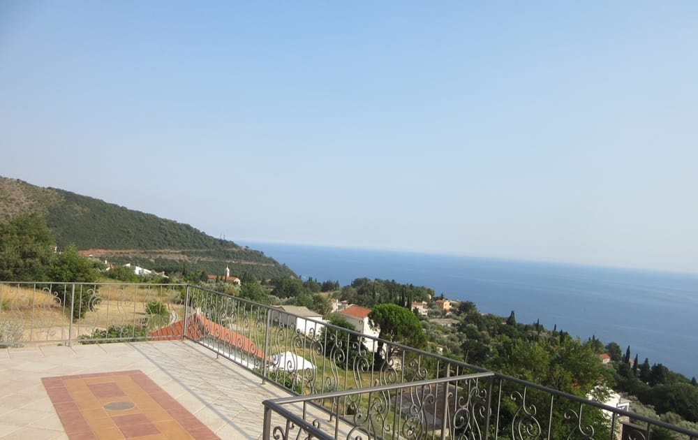 Vue panoramique sur la mer et les montagnes depuis la terrasse de la villa à Reževići, Monténégro : sol carrelé et garde-corps en fer forgé du balcon.