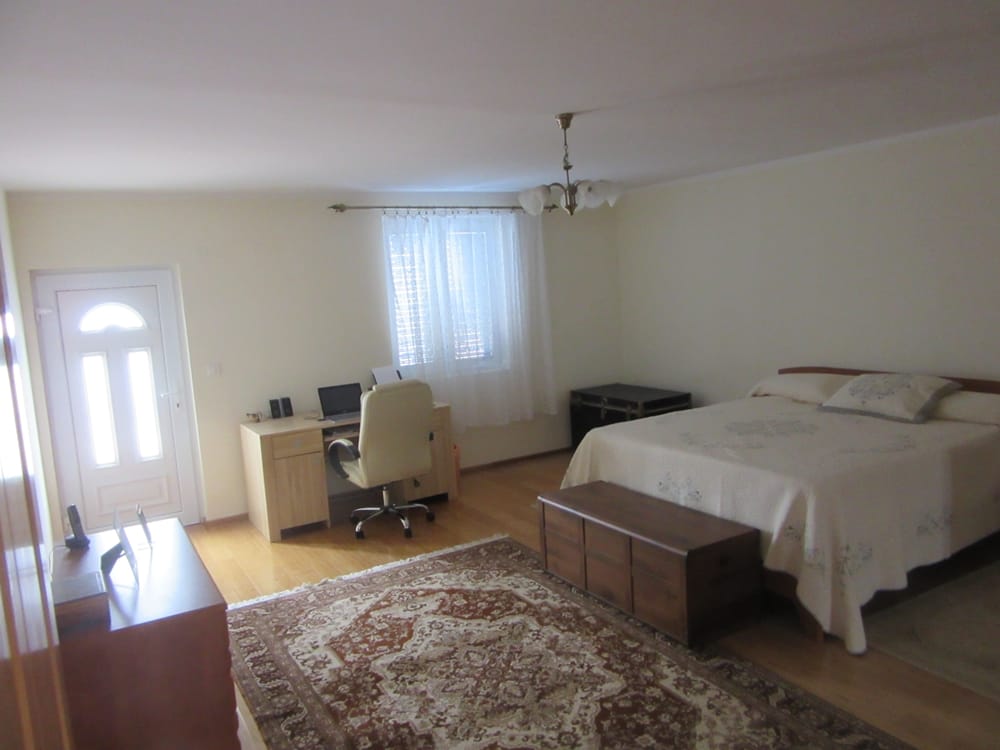 Chambre spacieuse avec lit double et espace de travail dans une villa à Reževići, Monténégro, avec parquet en bois.