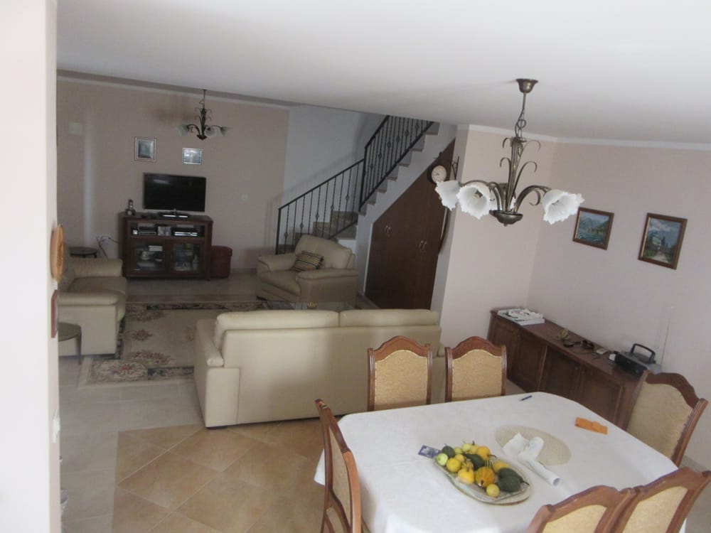 Salon spacieux avec coin repas dans une villa à Reževići, Monténégro : mobilier clair, escalier et décor classique.