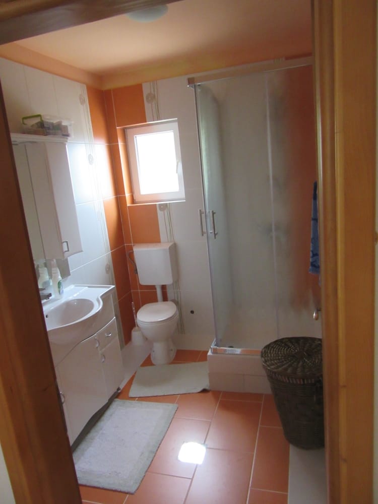 Salle de bains avec cabine de douche et carrelage orange dans une villa à Reževići, Monténégro : sanitaires et mobilier.