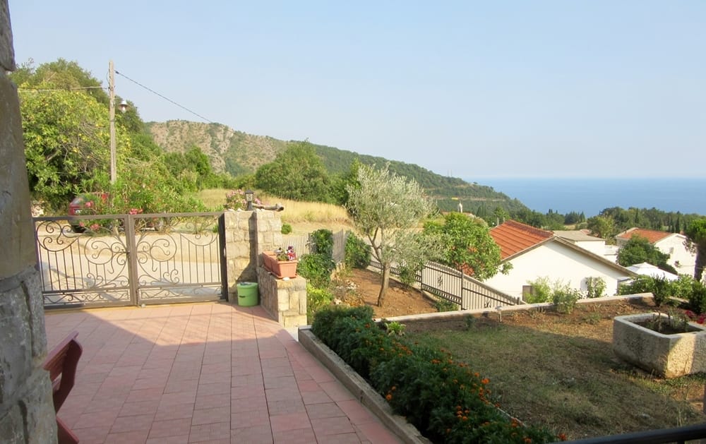 Terrasse de la villa à Reževići, Monténégro : vue sur la mer, les montagnes et un jardin soigné avec un olivier et une décoration en pierre.