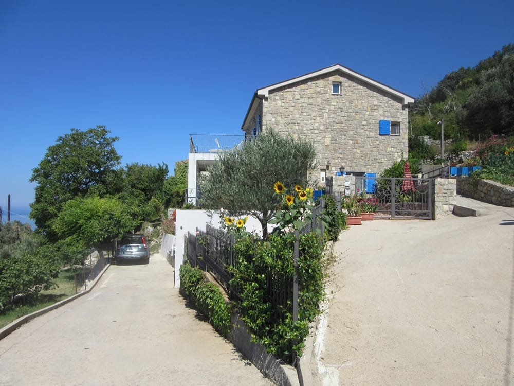Villa en pierre de deux étages à Reževići, Monténégro : façade en pierre naturelle, terrasse, jardin et parking devant la maison.