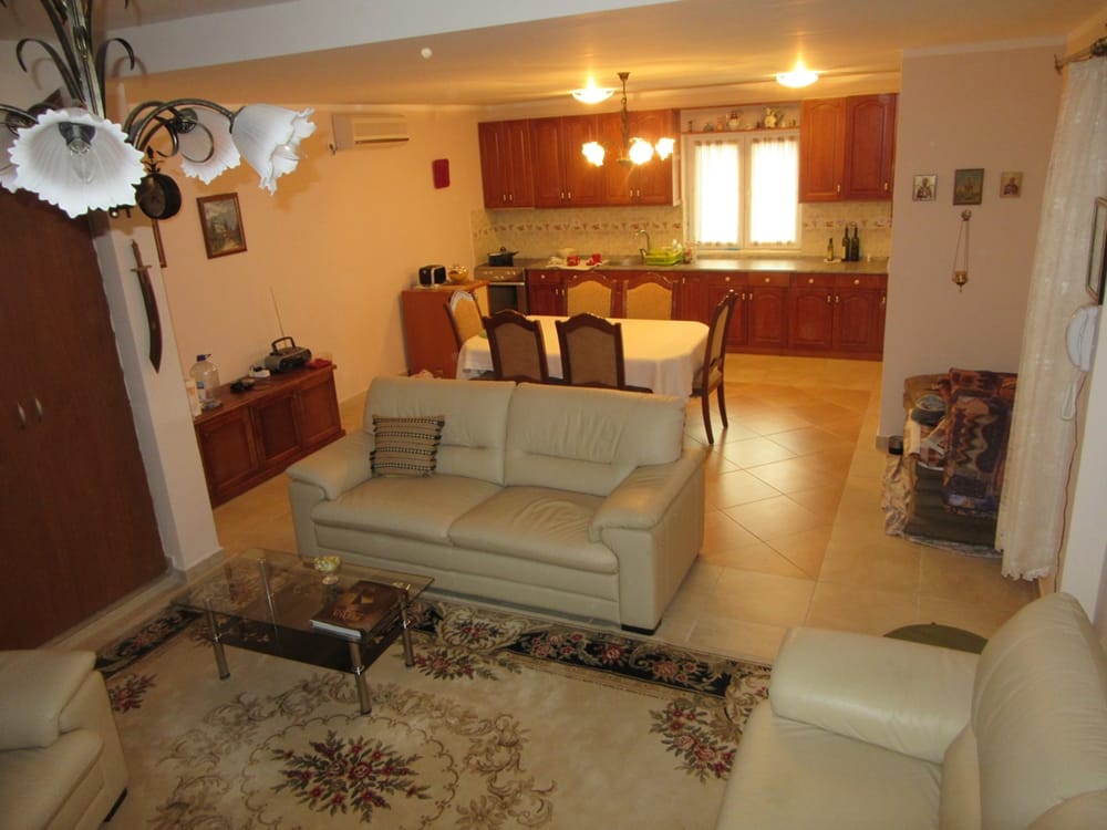 Salon avec cuisine dans une villa à Reževići, Monténégro : canapés en cuir clairs, coin repas et ensemble de cuisine en bois.