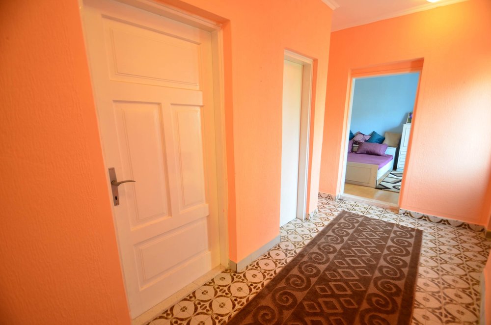 Flur im Haus in Herceg Novi, Montenegro: orange Wände, gefliester Boden mit Muster und Blick ins Schlafzimmer mit Bett.