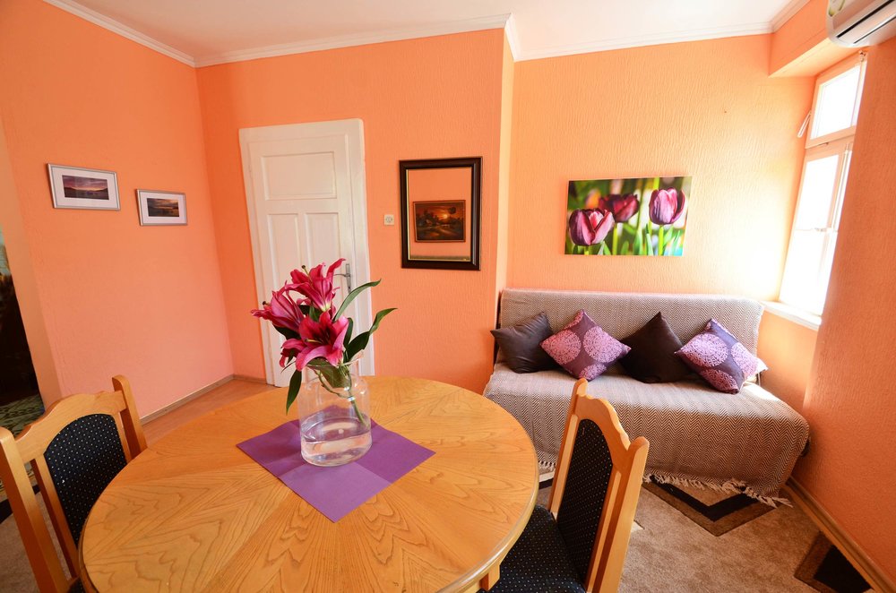 Gemütliches Wohnzimmer in einem Haus in Herceg Novi, Montenegro: Essbereich, Sofa mit Kissen und leuchtend orangefarbene Wände.