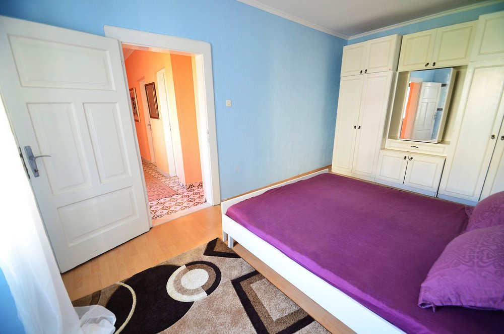 Schlafzimmer in einem Haus in Herceg Novi, Montenegro: Doppelbett mit violetter Bettwäsche, weißer Kleiderschrank und Teppich auf dem Boden.