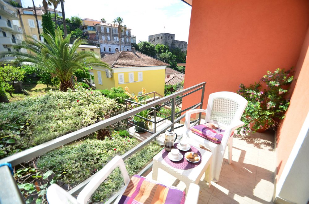 Gemütlicher Balkon mit Möbeln und Blick auf historische Architektur und einen Garten in Herceg Novi, Montenegro.