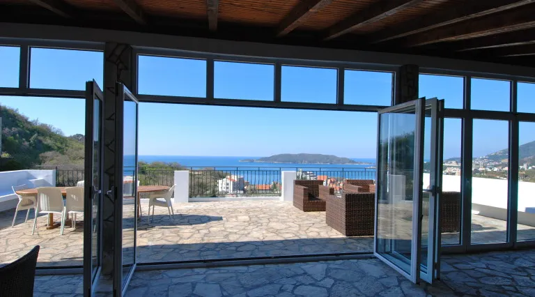 Terasa vile u Bečićima, Crna Gora: panoramski pogled na more, pleteni nameštaj i kamena obloga poda.