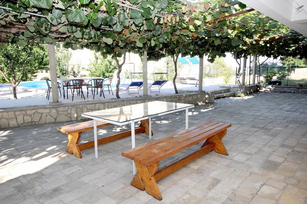 Terrasse des Hauses in Reževići, Montenegro: Steinboden, Holzbänke, Weinrebenüberdachung und Blick auf den Pool.