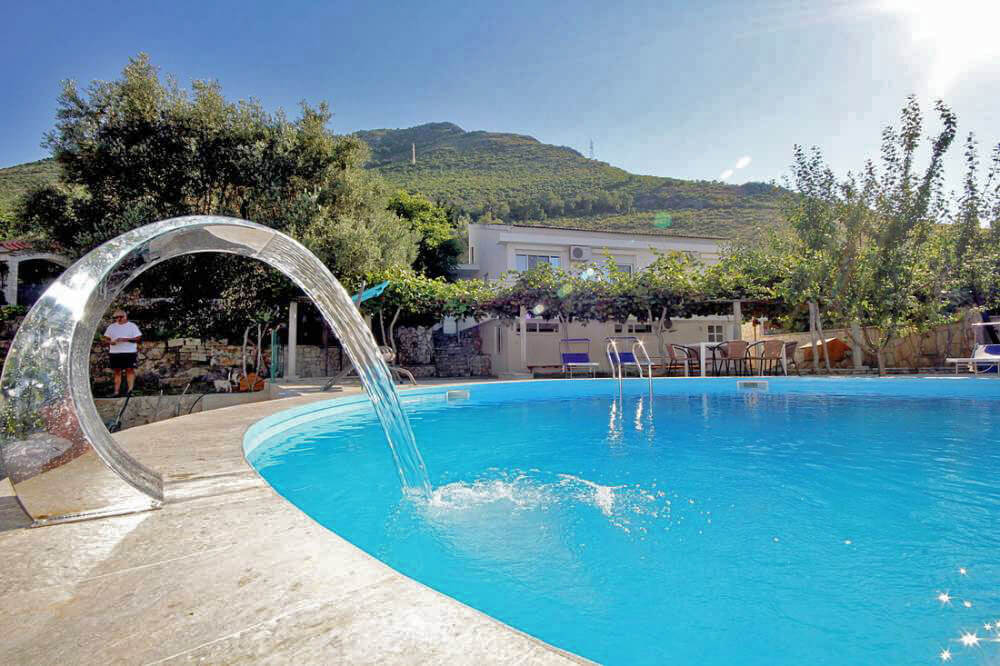 Reževići, Budva Rivierası, Karadağ’daki özel bir evin yanında, dağlar ve bahçe fonunda şelaleli açık yüzme havuzu.