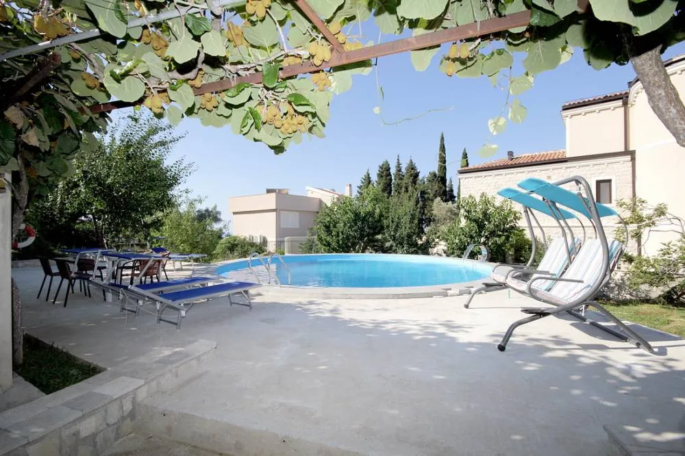 Offener Pool mit Liegestühlen und Schaukeln im Garten des Hauses in Reževići, Budva-Riviera, Montenegro, unter einem Kiwi-Dach.