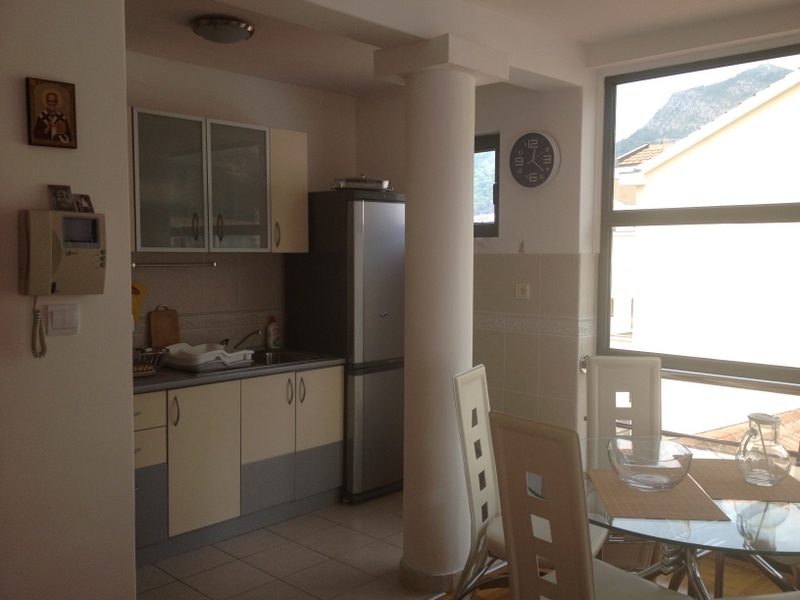 Küche mit Essbereich in einer Wohnung in Budva, Montenegro: helle Einbauküche, Essbereich und Panoramafenster mit Bergblick.