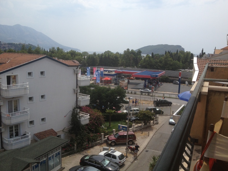 Blick vom Balkon einer Wohnung in Budva, Montenegro: Panorama der Stadt, Berge, Meer und städtische Infrastruktur mit Parkplatz.