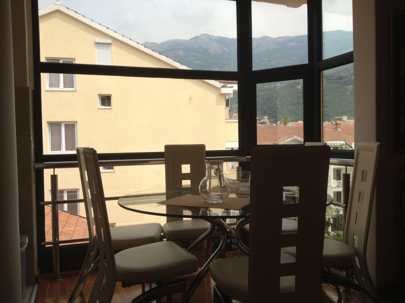 Essbereich mit Panoramablick auf die Berge in einer Wohnung in Budva, Montenegro: Glastisch und helle Stühle.