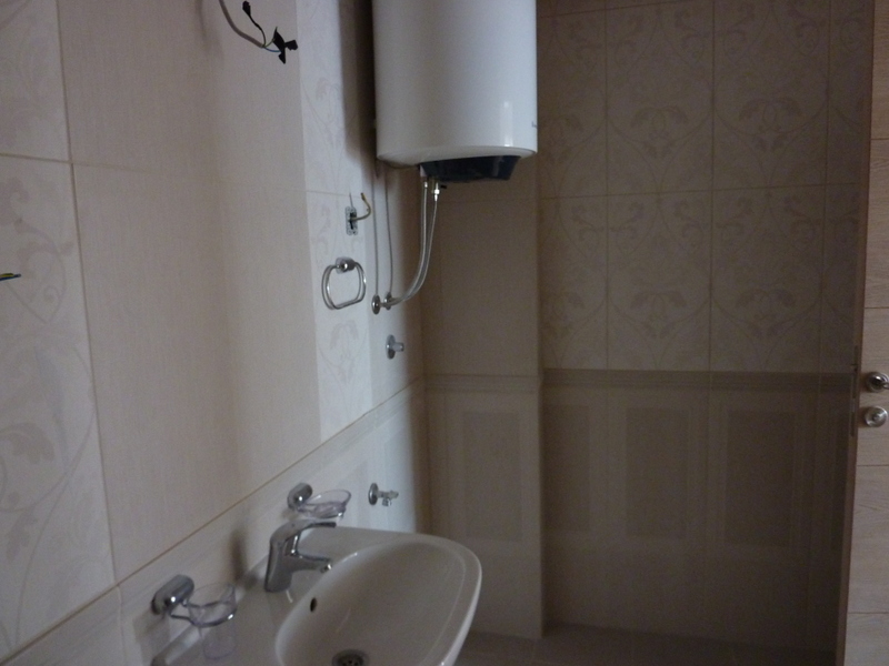 Kupatilo u stanu u Pržnu, Crna Gora: svetle pločice, instaliran bojler i lavabo sa slavinom.