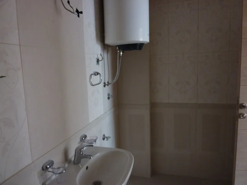 Badezimmer in einer Wohnung in Pržno, Montenegro: helle Fliesen, installierter Boiler und Waschbecken mit Armatur.