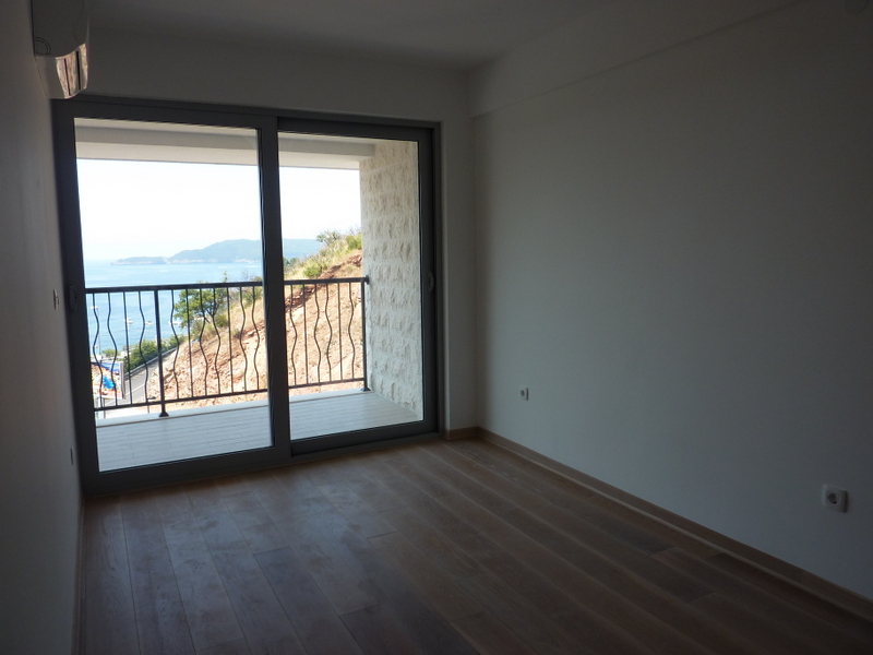 Svetao dnevni boravak u stanu u Pržnu, Crna Gora, sa panoramskim pogledom na more i izlazom na balkon sa kamenim oblogama.