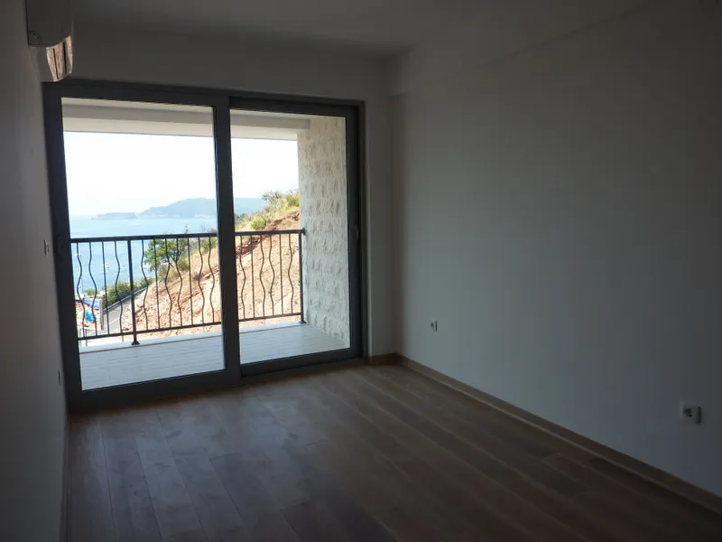 Helles Wohnzimmer in einer Wohnung in Pržno, Montenegro, mit Panoramablick auf das Meer und Zugang zu einem Balkon mit Steinverkleidung.