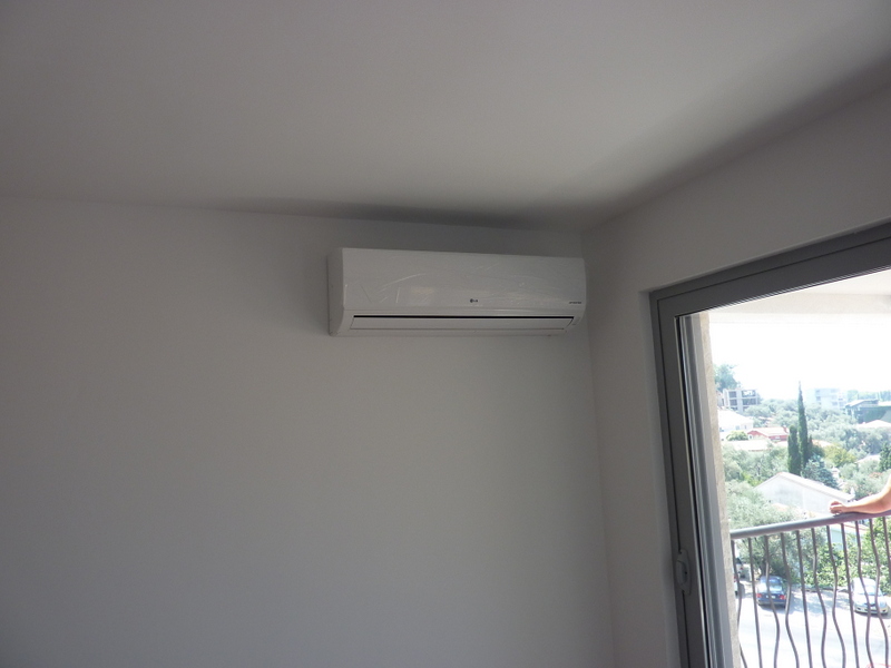 LG klima-uređaj u svetloj dnevnoj sobi stana u Pržnu, Crna Gora, sa izlazom na balkon i pogledom na zeleni pejzaž.
