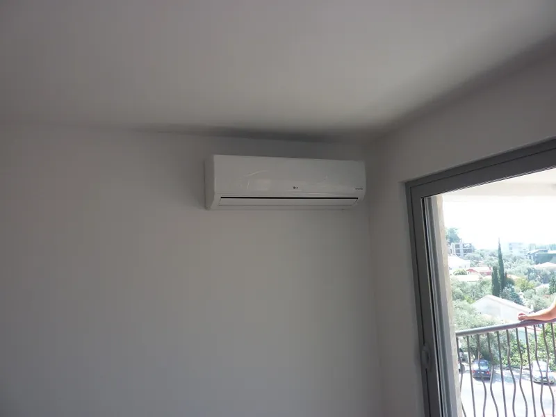 LG-Klimaanlage im hellen Wohnzimmer der Wohnung in Pržno, Montenegro, mit Zugang zum Balkon und Blick auf die grüne Landschaft.