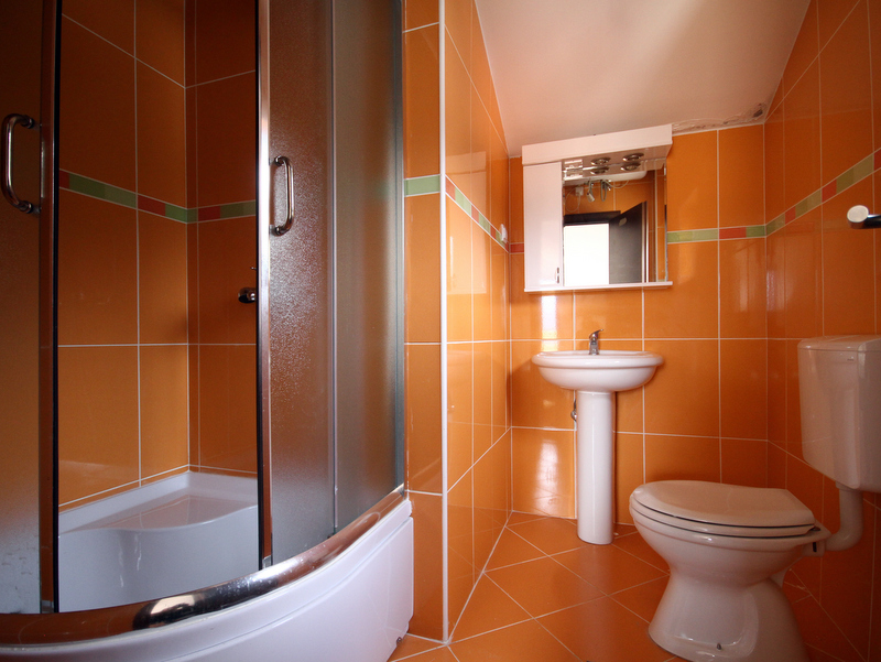 Badezimmer in einer Wohnung in Bečići, Montenegro: orangefarbene Fliesen, Duschkabine, Waschbecken und Toilette.