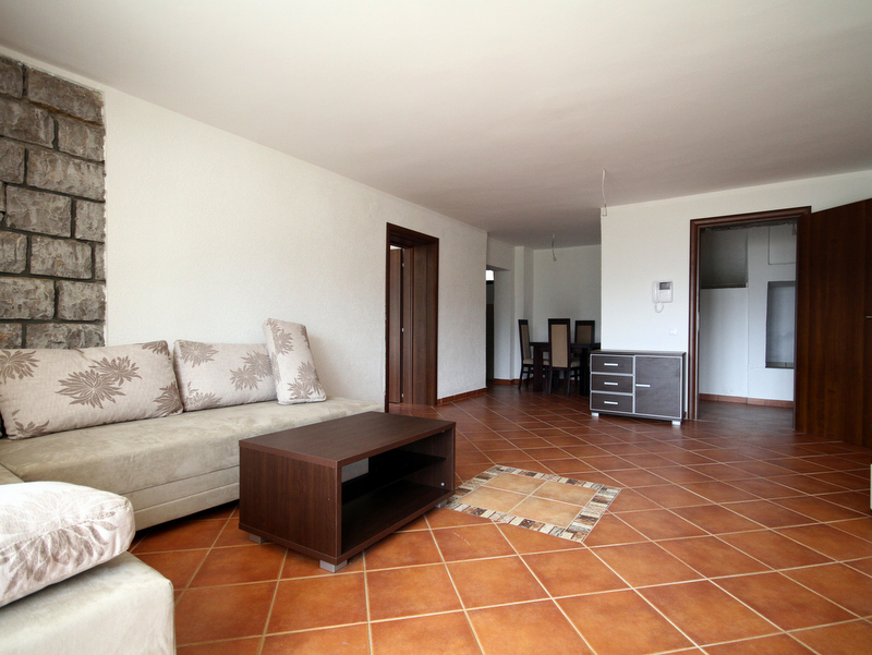 Wohnzimmer in einer Wohnung in Bečići, Montenegro: heller Raum mit Steinverkleidung an der Wand, weichem Sofa und Essbereich.