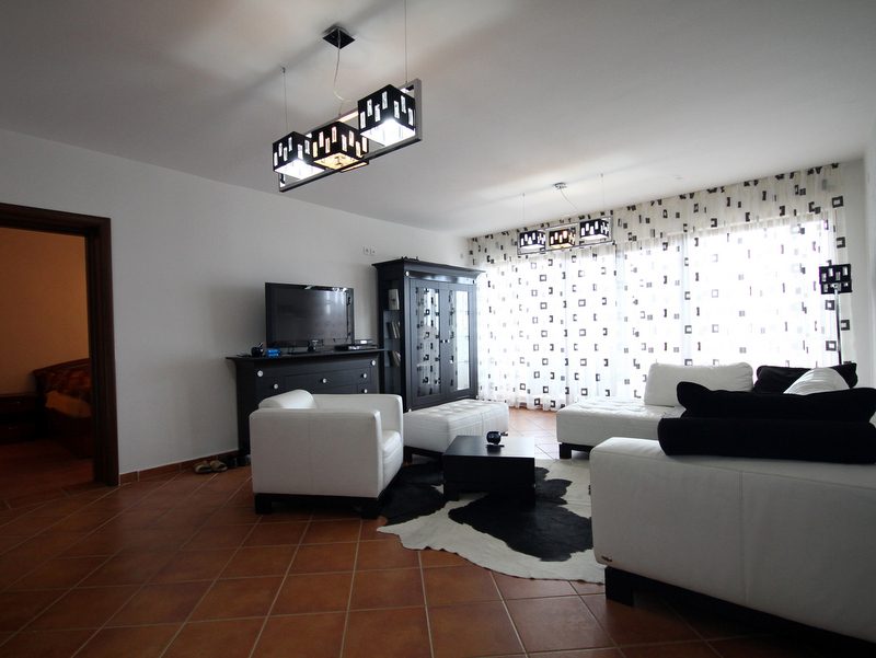 Wohnzimmer in einer Wohnung in Bečići, Montenegro: weiße Polstermöbel, schwarzer Schrank, Fliesenboden und Zebra-Teppich.