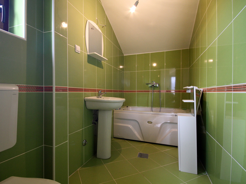 Badezimmer in einer Wohnung in Bečići, Montenegro: grüne Fliesen, weiße Sanitärkeramik, Badewanne und Spiegel im Interieur.