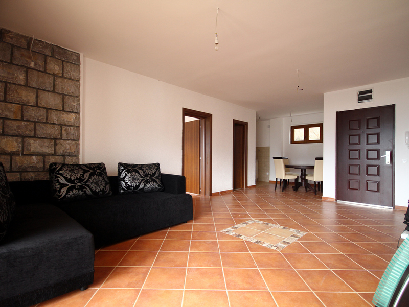 Wohnzimmer in einer Wohnung in Bečići, Montenegro: schwarzes Sofa, Steinwand, Fliesenboden und Essbereich.