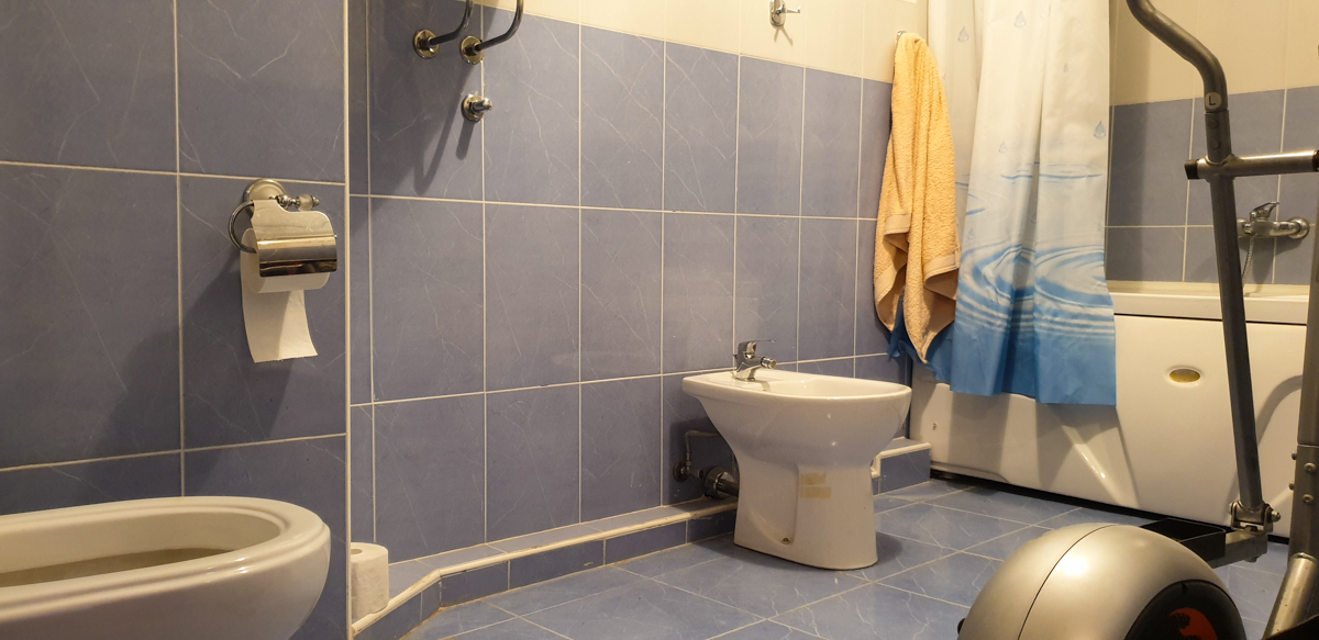 Kupatilo u stanu u Baru, Crna Gora: plave pločice, bide, kada sa zavesom i sprava za vežbanje u enterijeru.