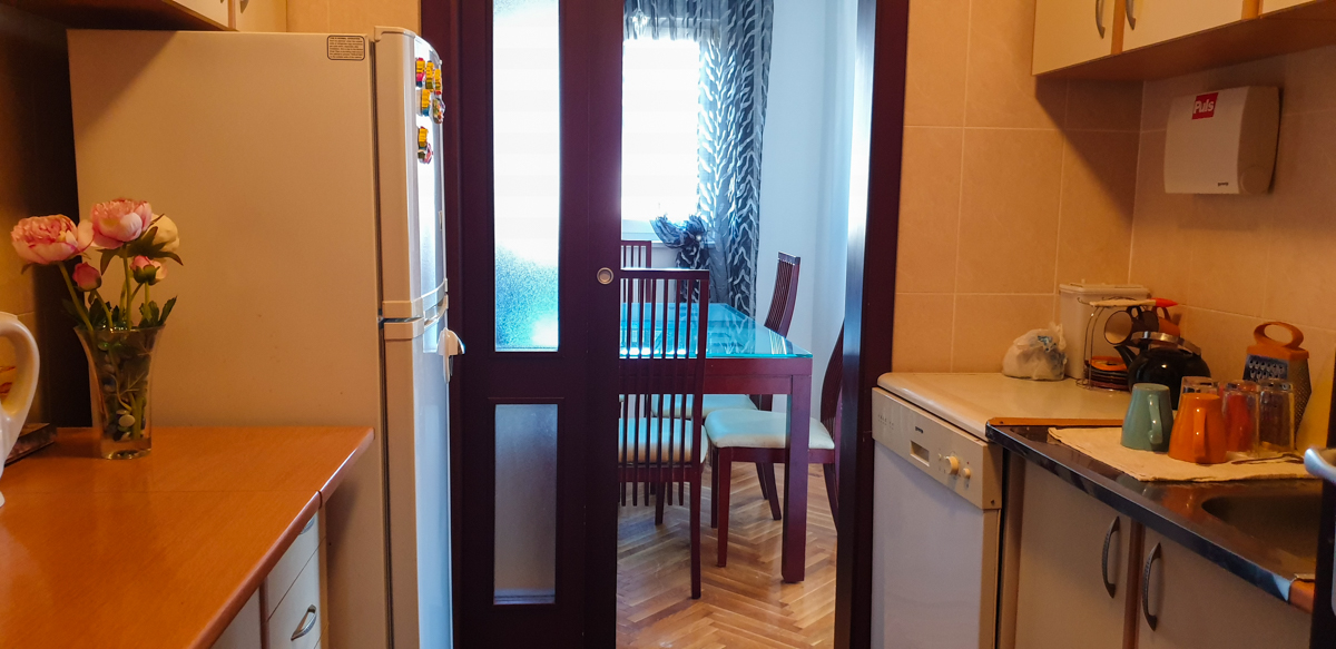 Kuhinja sa kućnim aparatima i trpezarijskim delom u stanu, grad Bar, Crna Gora. Pogled na trpezariju kroz staklena vrata.