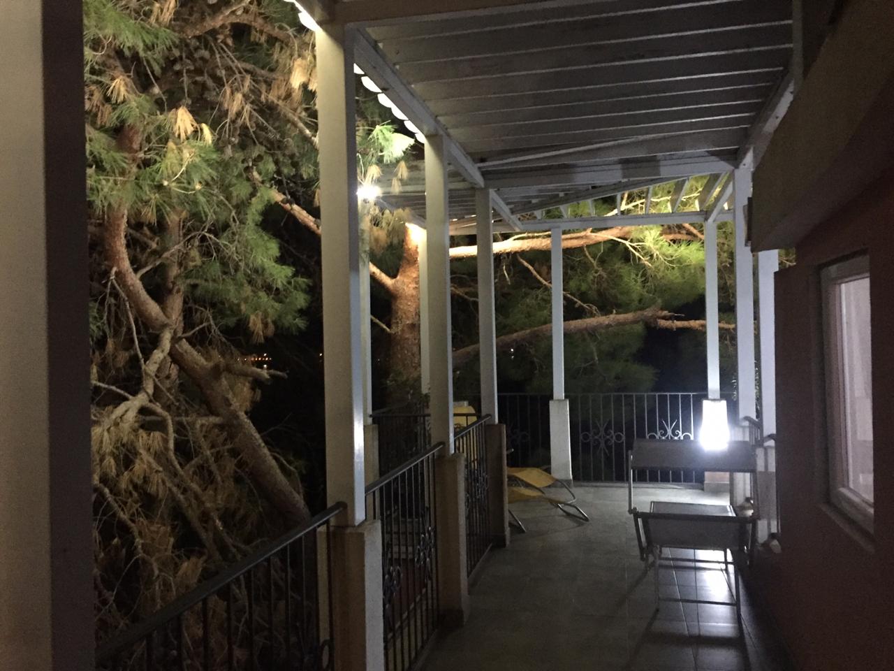 Gemütliche Terrasse mit Überdachung und Gartenmöbeln am Haus in Šušanj, Montenegro, mit Blick auf Kiefern im Abendlicht.