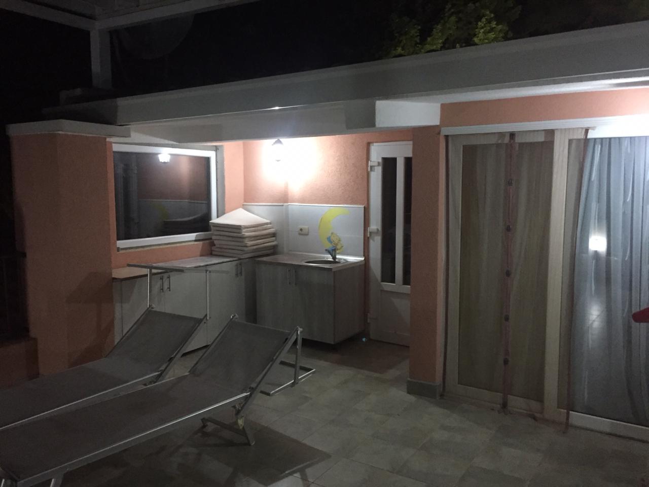 Terrasse des Hauses in Šušanj, Montenegro: Sommerküche, Liegestühle und Panoramaverglasung am Abend.